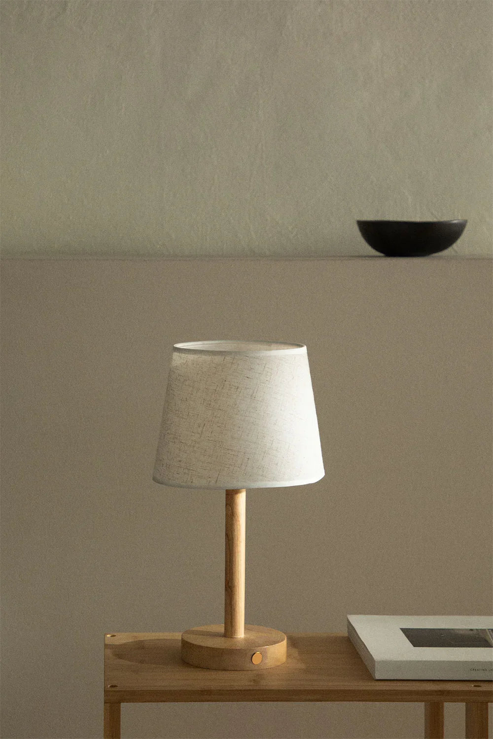 Een draadloze tafellamp van Ambiora met een minimalistisch ontwerp. De lamp heeft een houten voet en een stijlvolle linnen lampenkap, met een eenvoudige bedieningsknop aan de onderkant. Het moderne, minimalistische ontwerp zorgt voor een rustige en verfijnde sfeer in elke ruimte.