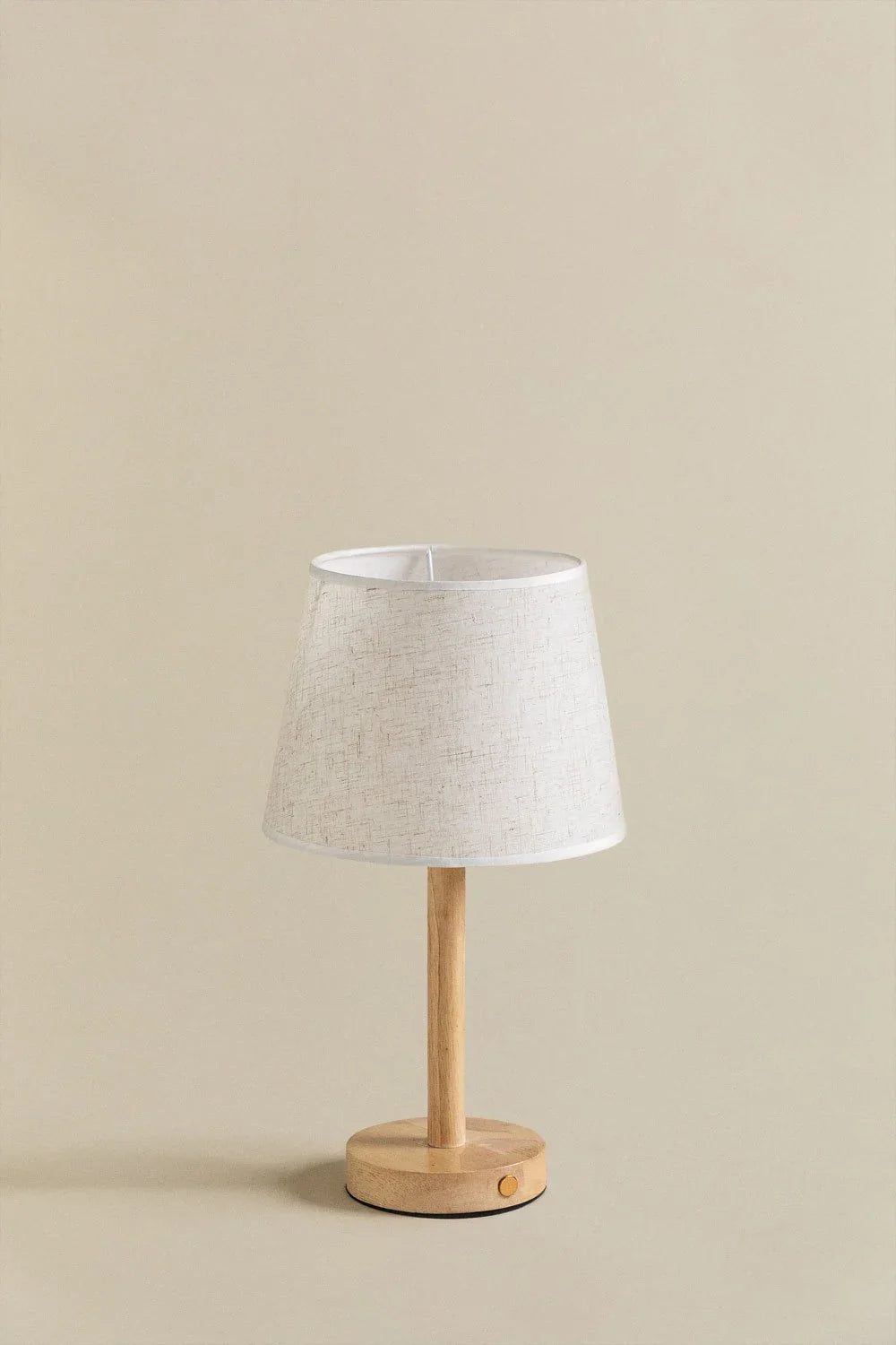 Een draadloze tafellamp van Ambiora met een minimalistisch ontwerp. De lamp heeft een houten voet met een stijlvolle linnen lampenkap en een knop aan de basis voor eenvoudige bediening, die een warme en gezellige sfeer creëert in elke ruimte.