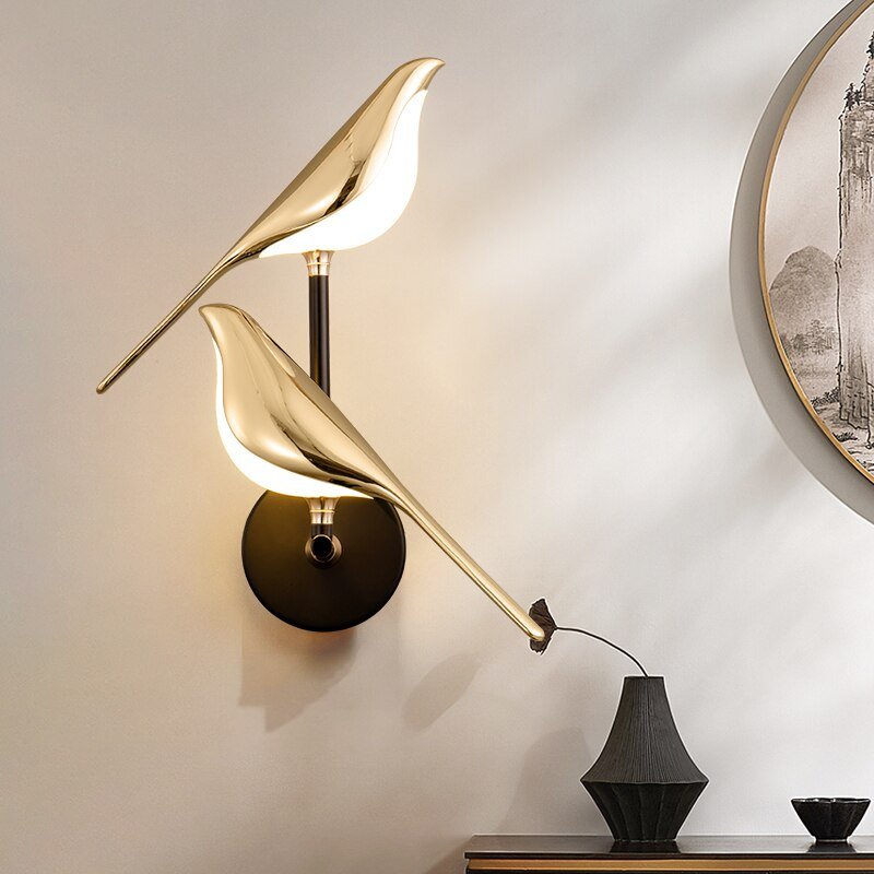 Auroria wandlamp met een dubbel vogelontwerp in glanzend goud, bevestigd op een stijlvolle zwarte basis, biedt een artistieke en sfeervolle verlichting voor moderne en elegante interieurs.