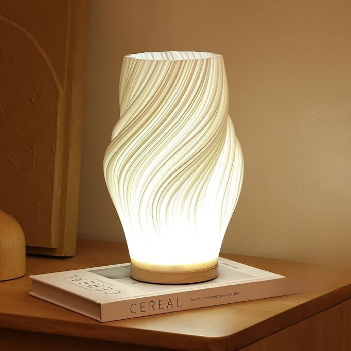 Balaara Serene Wavecrest Lamp in kalme, witte kleur met een golvende structuur, verlicht op een boekenplank, waardoor een rustgevende sfeer ontstaat.